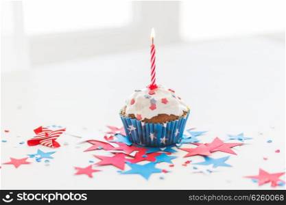 independence day, celebration, patriotism and holidays concept - close up of glazed cupcake or muffin with burning candle and stars cofetti decoration on table at 4th july party