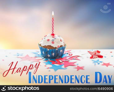 independence day, celebration, patriotism and holidays concept - close up of glazed cupcake or muffin with burning candle and stars cofetti on table at 4th july party over evening sky background. cupcake with candle on american independence day. cupcake with candle on american independence day