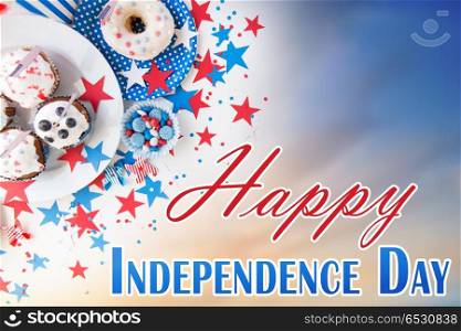 independence day, celebration, patriotism and holidays concept - close up of glazed cupcakes or muffins decorated with american flags, donut and red blue candies at 4th july party. cupcakes with american flags on independence day. cupcakes with american flags on independence day