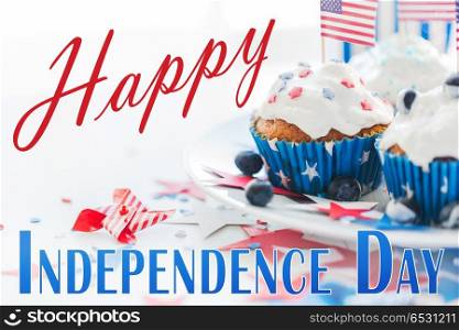 independence day, celebration, patriotism and holidays concept - close up of glazed cupcakes or muffins decorated with american flags and blueberries at party 4th of july. cupcakes with american flags on independence day. cupcakes with american flags on independence day
