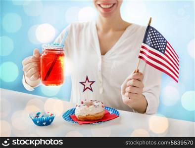 independence day, celebration, patriotism and holidays concept - close up of happy woman with donut celebrating 4th july, holding american flag and drinking juice over blue lights background