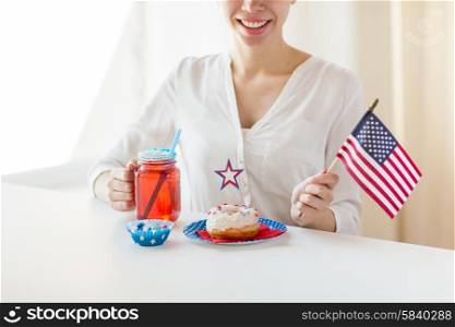 independence day, celebration, patriotism and holidays concept - close up of happy woman with donut celebrating 4th july, holding american flag and drinking juice from glass mason jar or mug at home