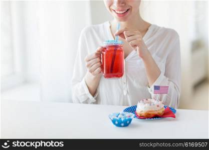 independence day, celebration, patriotism and holidays concept - close up of happy woman eating glazed sweet donut, drinking juice from glass mason jar or mug and celebrating 4th july at home party
