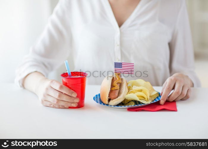 independence day, celebration, patriotism and holidays concept - close up of woman eating hot dog with american flag decoration and potato chips, drinking juice and celebrating 4th july at home party