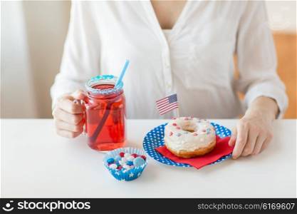 independence day, celebration, patriotism and holidays concept - close up of woman eating glazed sweet donut, drinking juice from big glass mason jar or mug and celebrating 4th july at home party