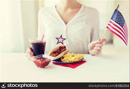 independence day, celebration, patriotism and holidays concept - close up of woman hands with hot dog and french fries holding american flag and cola drink on 4th july at home party