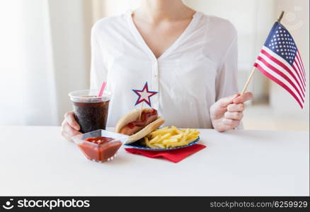 independence day, celebration, patriotism and holidays concept - close up of woman hands with hot dog and french fries holding american flag and coca cola drink on 4th july at home party