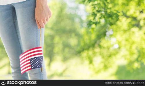 independence day, celebration, patriotism and holidays concept - close up of woman legs and hand holding american flag at 4th july over green natural background. close up of woman holding american flag in hand