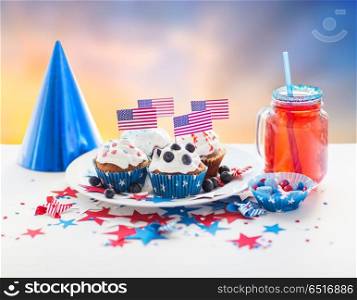 independence day, celebration, patriotism and holidays concept - glazed cupcakes or muffins decorated with american flags, candies and berry lemonade drink in mason jar at party 4th of july. cupcakes with american flags on independence day. cupcakes with american flags on independence day