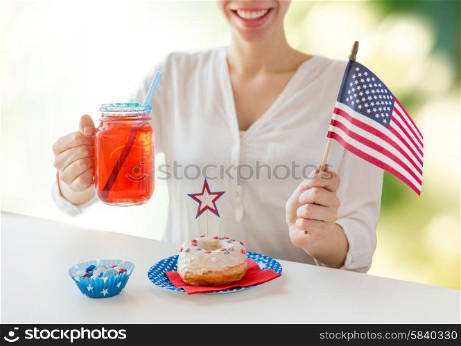independence day celebration, patriotism and holidays concept - happy woman with donut celebrating 4th july, holding american flag and drinking juice from glass mason jar over green background