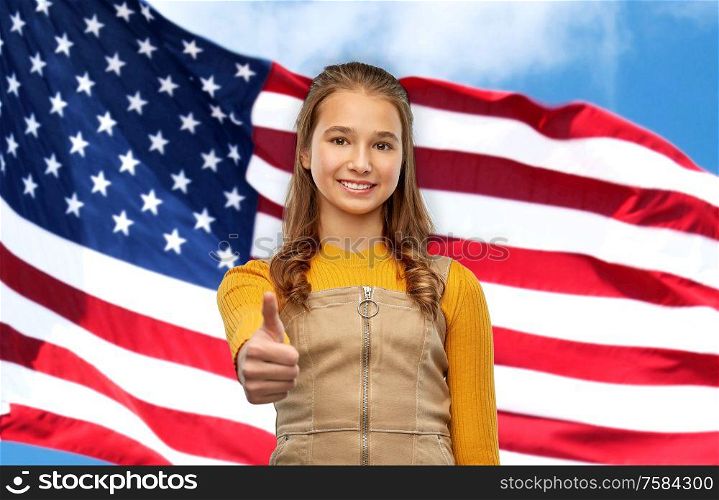 independence day, gesture and patriotism concept - smiling young teenage girl showing thumbs up over american flag background. teenage girl showing thumbs up over american flag