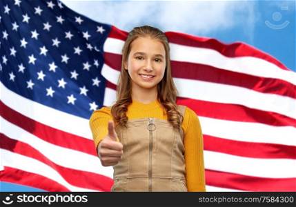 independence day, gesture and patriotism concept - smiling young teenage girl showing thumbs up over american flag background. teenage girl showing thumbs up over american flag
