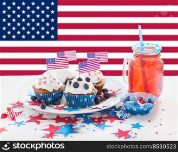 independence day, patriotism and holidays concept - close up of iced cupcakes, juice glass or mason jar and candies at 4th july party over flag of united states of america on background. cupcakes with american flags on independence day