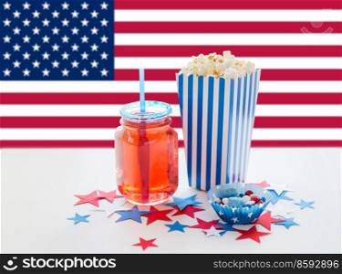 independence day, patriotism and holidays concept - close up of popcorn, juice in mason jar glass and candies at 4th july party over flag of united states of america on background. food and drink on american independence day party