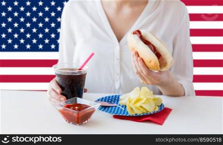 independence day, patriotism and holidays concept - close up of woman eating hot dog and drinking cola at 4th july at party over flag of united states of america on background. close up of woman eating hotdog with cola