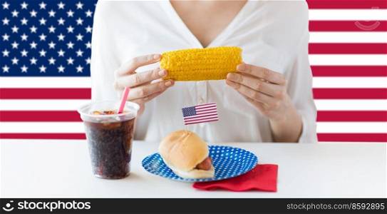independence day, patriotism and holidays concept - close up of woman eating corn and hot dog with cola on 4th july party over flag of united states of america on background. woman eating corn at independence day party