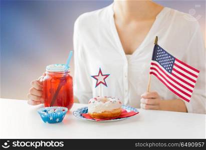 independence day, patriotism and holidays concept - close up of woman with american flag and donut celebrating 4th july and drinking berry lemonade from glass mason jar over evening sky background. woman celebrating american independence day. woman celebrating american independence day