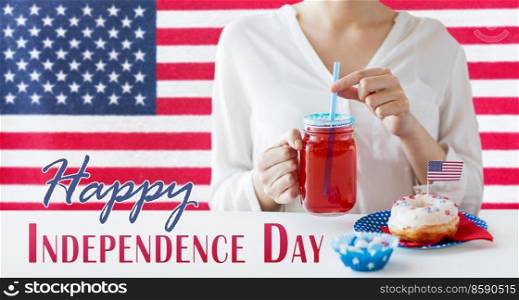 independence day, patriotism and holidays concept - close up of woman with iced donut drinking juice from mason jar glass or mug at 4th july party over flag of united states of america on background. woman celebrating american independence day