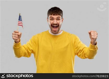 independence day, patriotism and national people concept - happy laughing young man in yellow sweatshirt with flag of america celebrating success over grey background. happy laughing man with flag of america