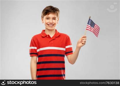 independence day, patriotism and people concept - portrait of happy smiling boy in red polo t-shirt holding flag of united states of america over grey background. portrait of happy smiling boy in red polo t-shirt