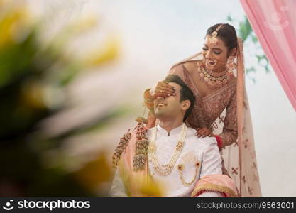 Indian beautiful bride covering her groom's eyes with hands 