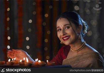 Indian beautiful lady posing in front of camera by covering the flame of diyas with hand on the occasion of Diwali