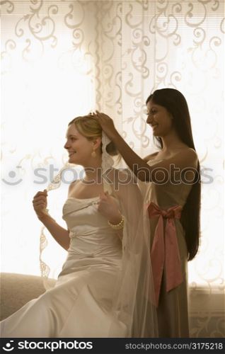 Indian bridesmaid placing veil on Caucasian bride.