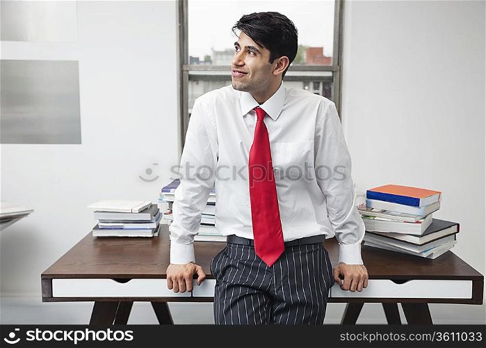 Indian businessman leaning on desk while looking away in office