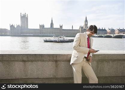 Indian businessman text messaging with watercraft and buildings in background