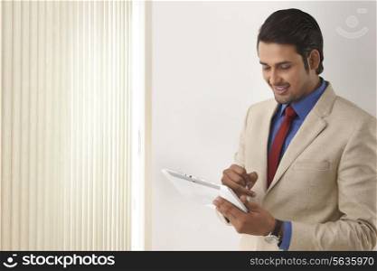 Indian businessman using digital tablet by window blinds