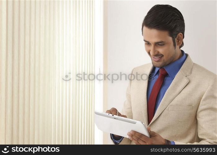 Indian businessman using tablet computer by window blinds