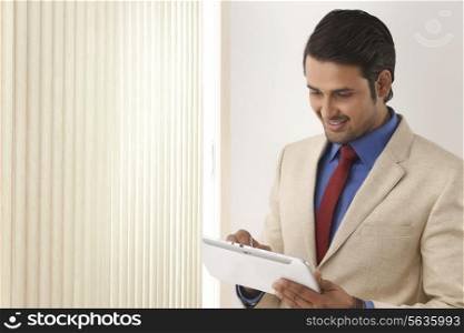 Indian businessman using tablet computer by window blinds