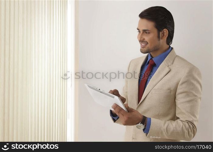Indian businessman using tablet PC by window blinds