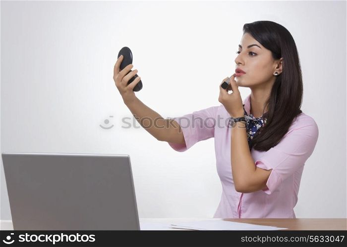 Indian businesswoman applying lipstick at office desk