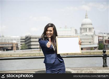Indian businesswoman gesturing thumbs up as she holds Moodboard sign with St. Paul&acute;s Cathedral in background