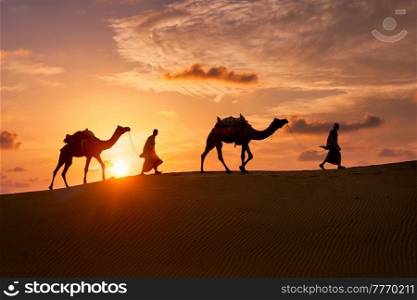 Indian cameleers (camel driver) bedouin with camel silhouettes in sand dunes of Thar desert on sunset. Caravan in Rajasthan travel tourism background safari adventure. Jaisalmer, Rajasthan, India. Indian cameleers camel driver with camel silhouettes in dunes on sunset. Jaisalmer, Rajasthan, India