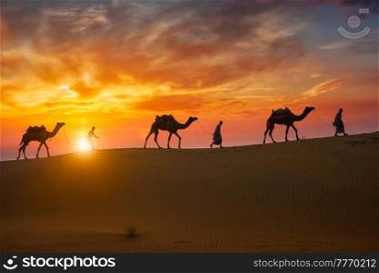 Indian cameleers (camel driver) bedouin with camel silhouettes in sand dunes of Thar desert on sunset. Caravan in Rajasthan travel tourism background safari adventure. Jaisalmer, Rajasthan, India. Indian cameleers camel driver with camel silhouettes in dunes on sunset. Jaisalmer, Rajasthan, India