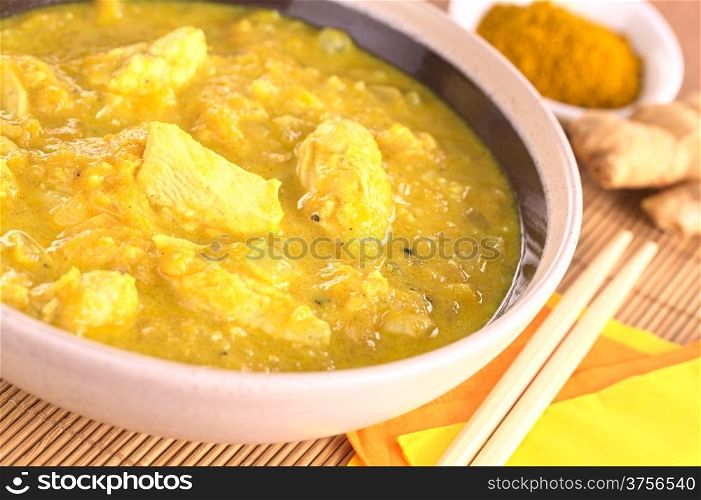 Indian chicken-mango curry dish in bowl with curry powder and ginger root in the back (Selective Focus, Focus on the horizontal chicken piece in the middle of the bowl)