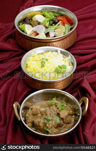 Indian copper dishes with beef rogan josh, white and yellow rice and a salad, shot with a tilt-shift lens to hold focus from front to back.