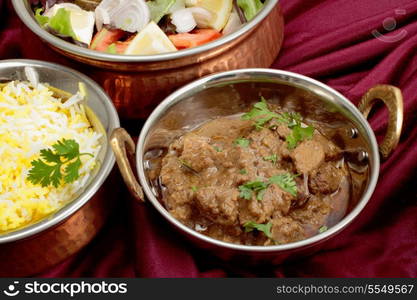 Indian copper dishes with beef rogan josh, white and yellow rice and a salad, shot with a tilt-shift lens to hold focus from front to back.