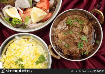 Indian copper dishes with homemade beef rogan josh, white and yellow rice and a salad, seen from above