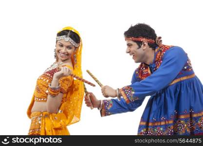 Indian couple in traditional wear performing Dandiya Raas over white background