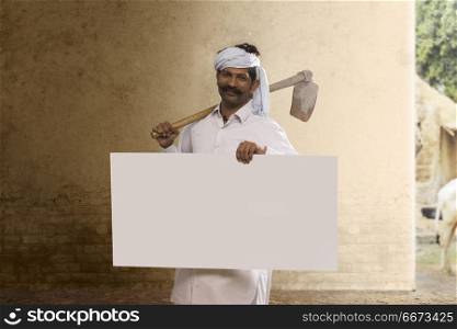 Indian farmer carrying hoe on his shoulder and holding placard