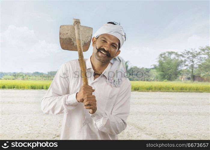 Indian farmer carrying hoe on his shoulder standing in field
