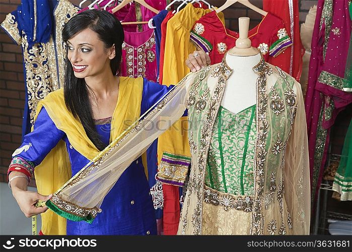 Indian female dressmaker measuring traditional outfit at design studio