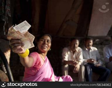 Indian female vendor holding banknotes with customers sitting in background
