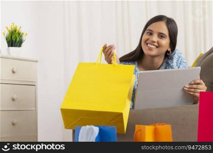 Indian girl in happy mood lying on sofa with shopping bag and tablet in her hands