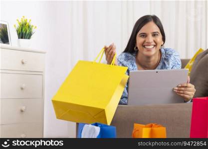 Indian girl in happy mood lying on sofa with shopping bag and laptop in her hands