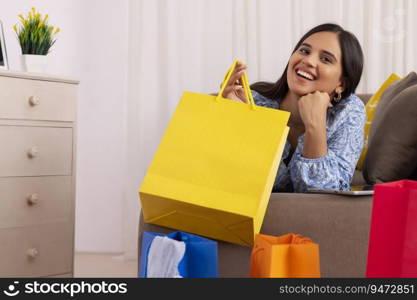 Indian girl in happy mood lying on sofa with shopping bag in her hand