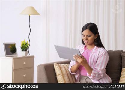 Indian girl looking at her tablet while sitting on sofa